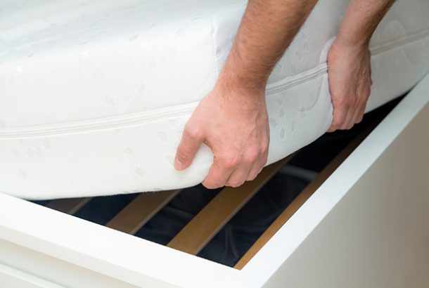Man hands lifting the mattress at the bedroom. Looking at the bed frame, inspects the mattress